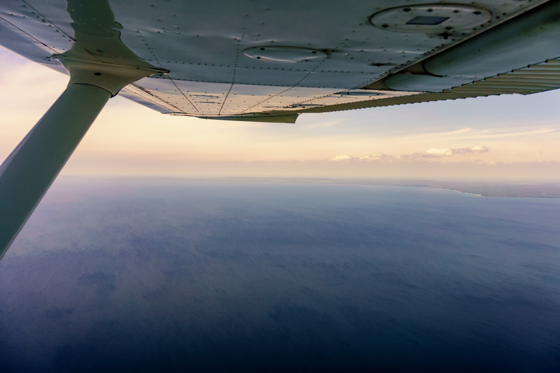 A Navy fighter jet banking over the ocean near an aircraft carrier