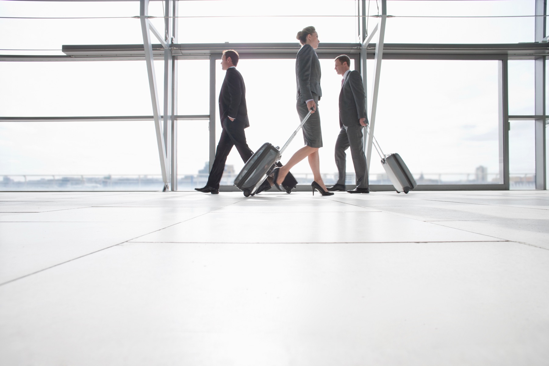An airport departure terminal with travelers and a rolling suitcase