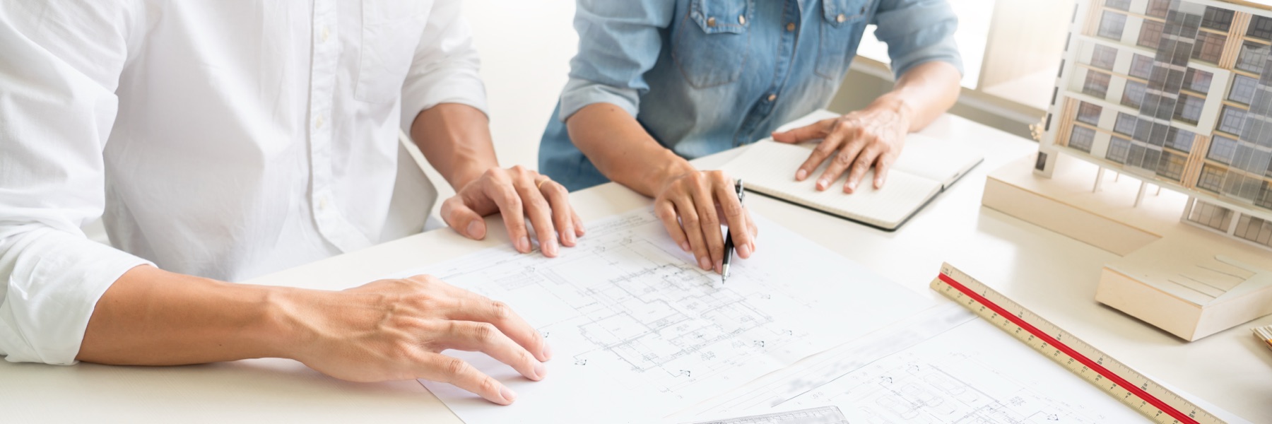 Two business representatives reviewing engineering blueprints across a conference table