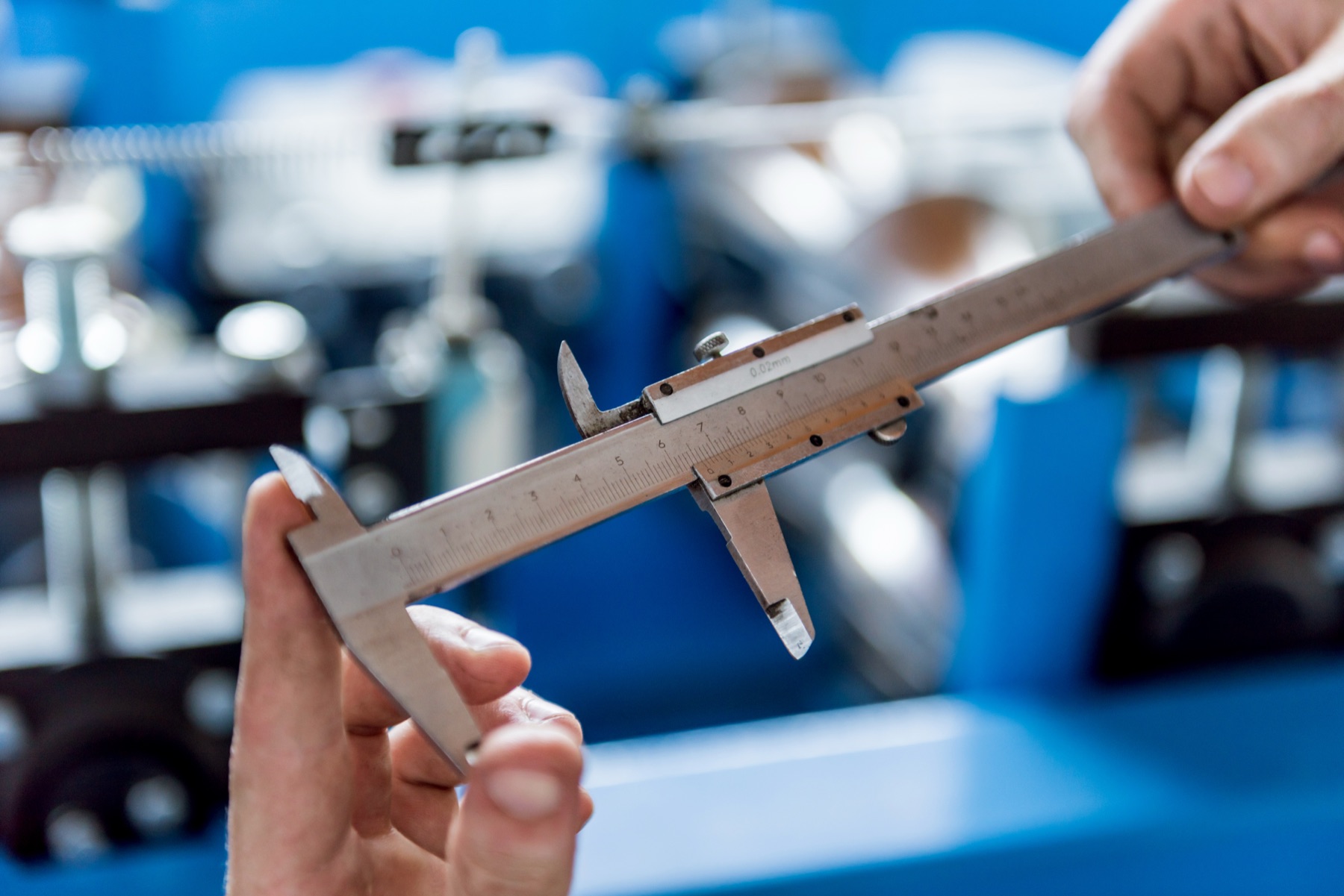 An engineer measuring a metal industrial nozzle with calipers at a workbench